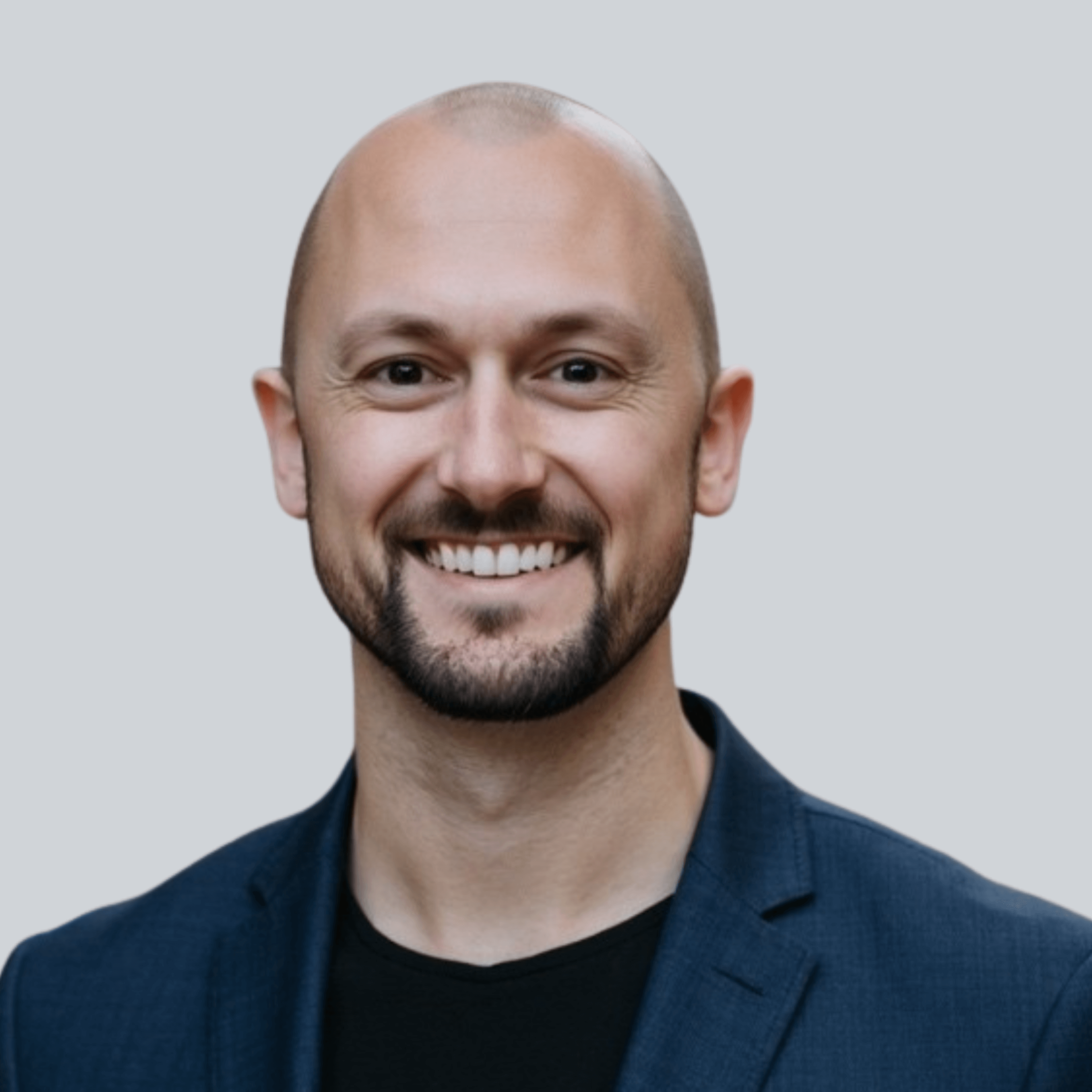 Photo of a smiling man dressed professionally standing against a gray background