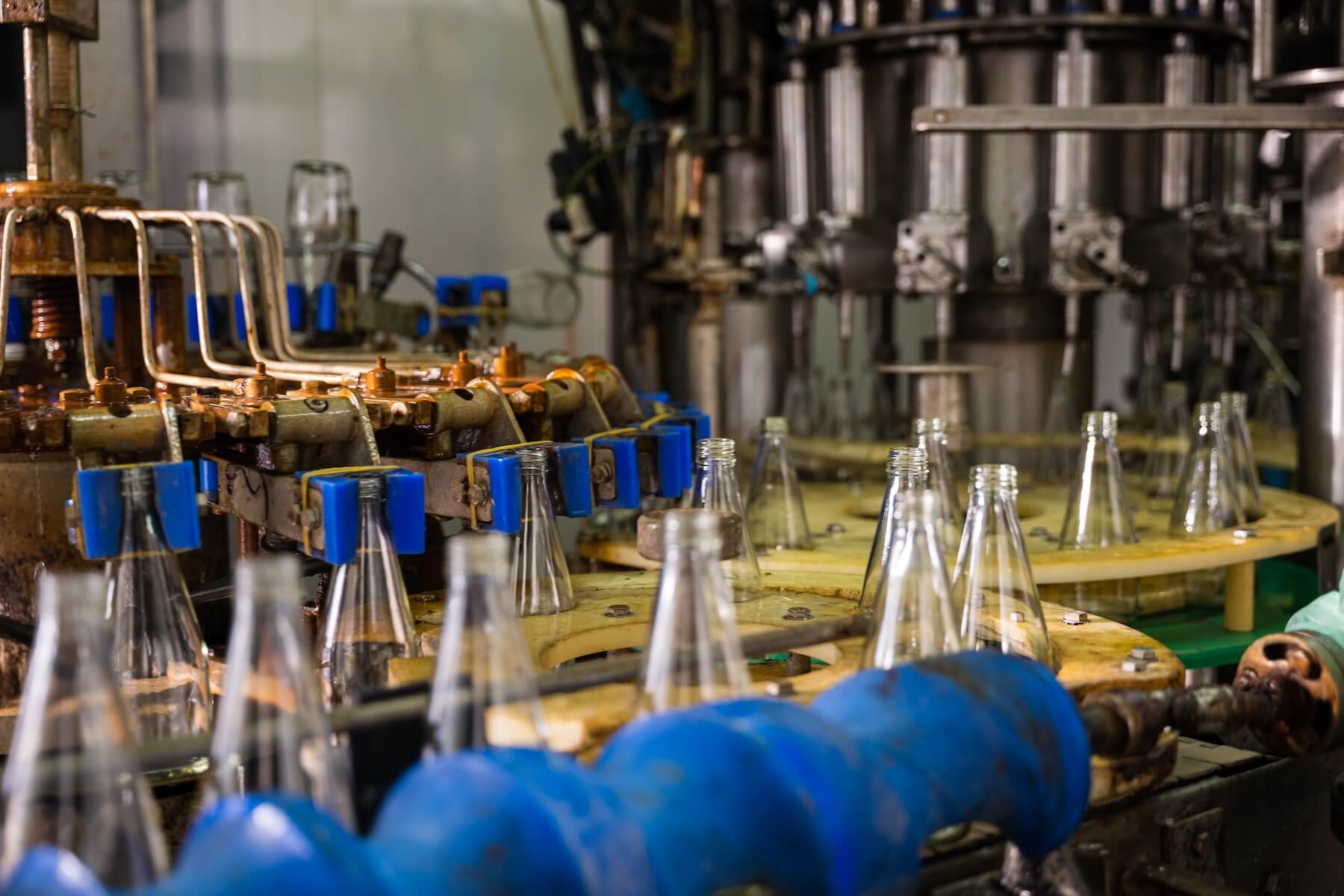 A conveyor in a modern distillery features empty glass bottles for alcoholic beverage production and bottling. The automated clean factory assures efficient manufacturing and multi-category cost tracking.