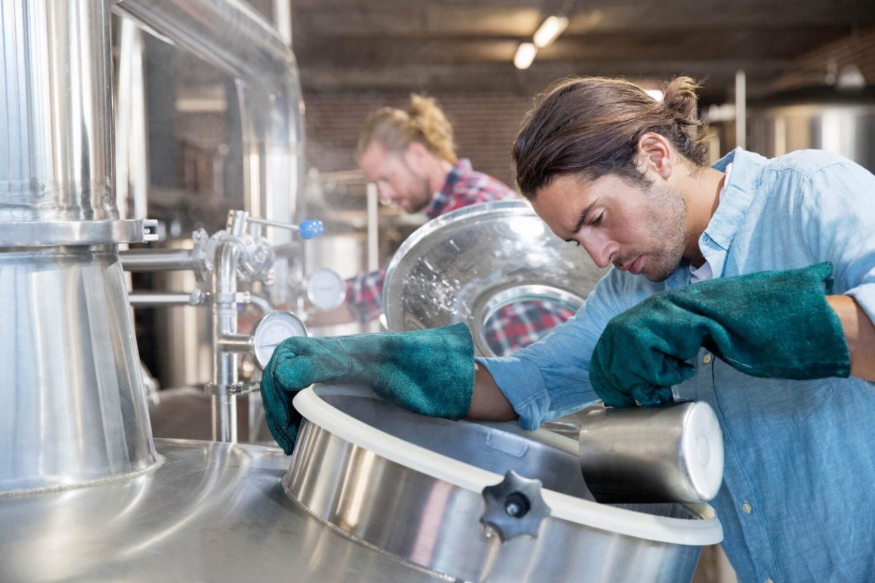 A photo of two brewery workings checking fermentation tanks while making non-alcoholic beer.