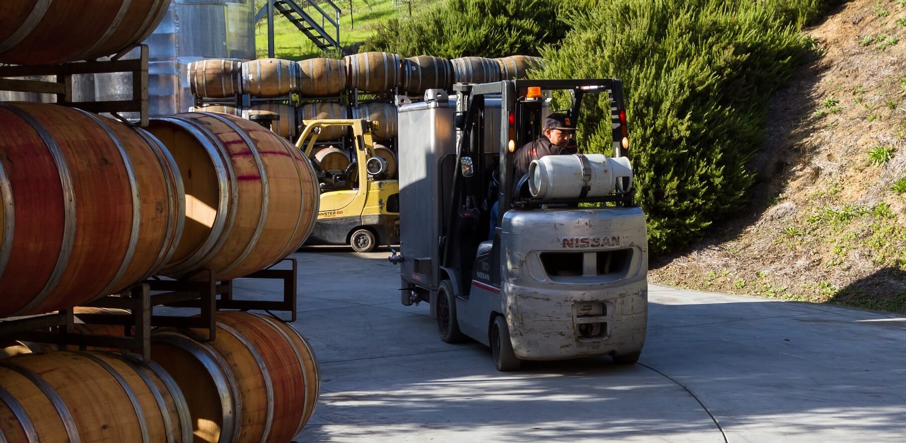 A photo of a man driving a forklift at a winery moving barrels from one location to another