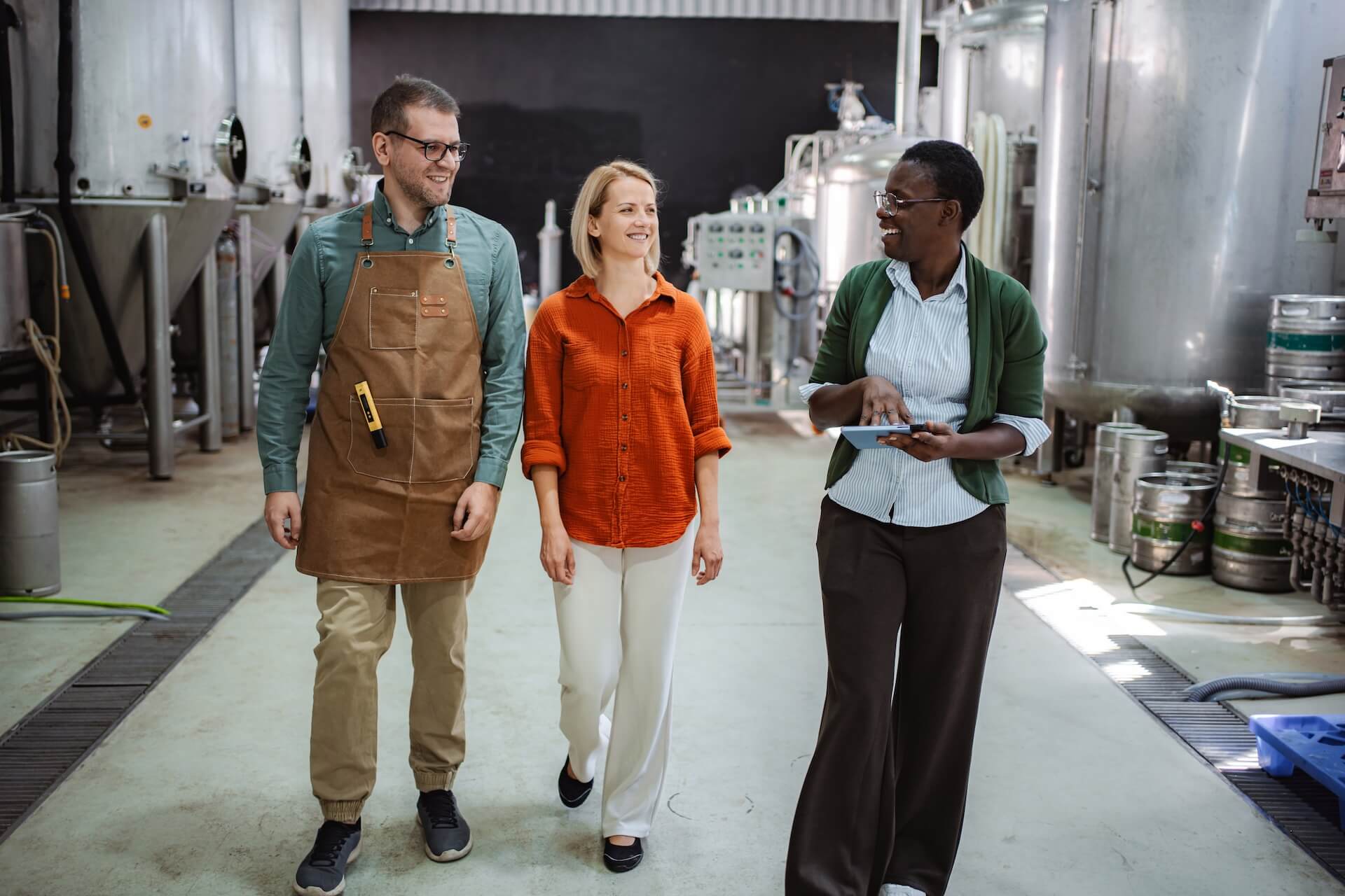 Three adults walking through a brewery, talking and reviewing information on a tablet