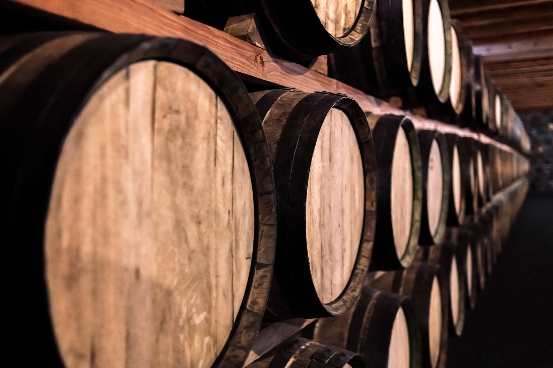 rows of wooden barrels on shelves with aging whiskey inside of them. Crafted ERP Mobile allows distillery production and warehouse teams to manage barrels where the work happens.