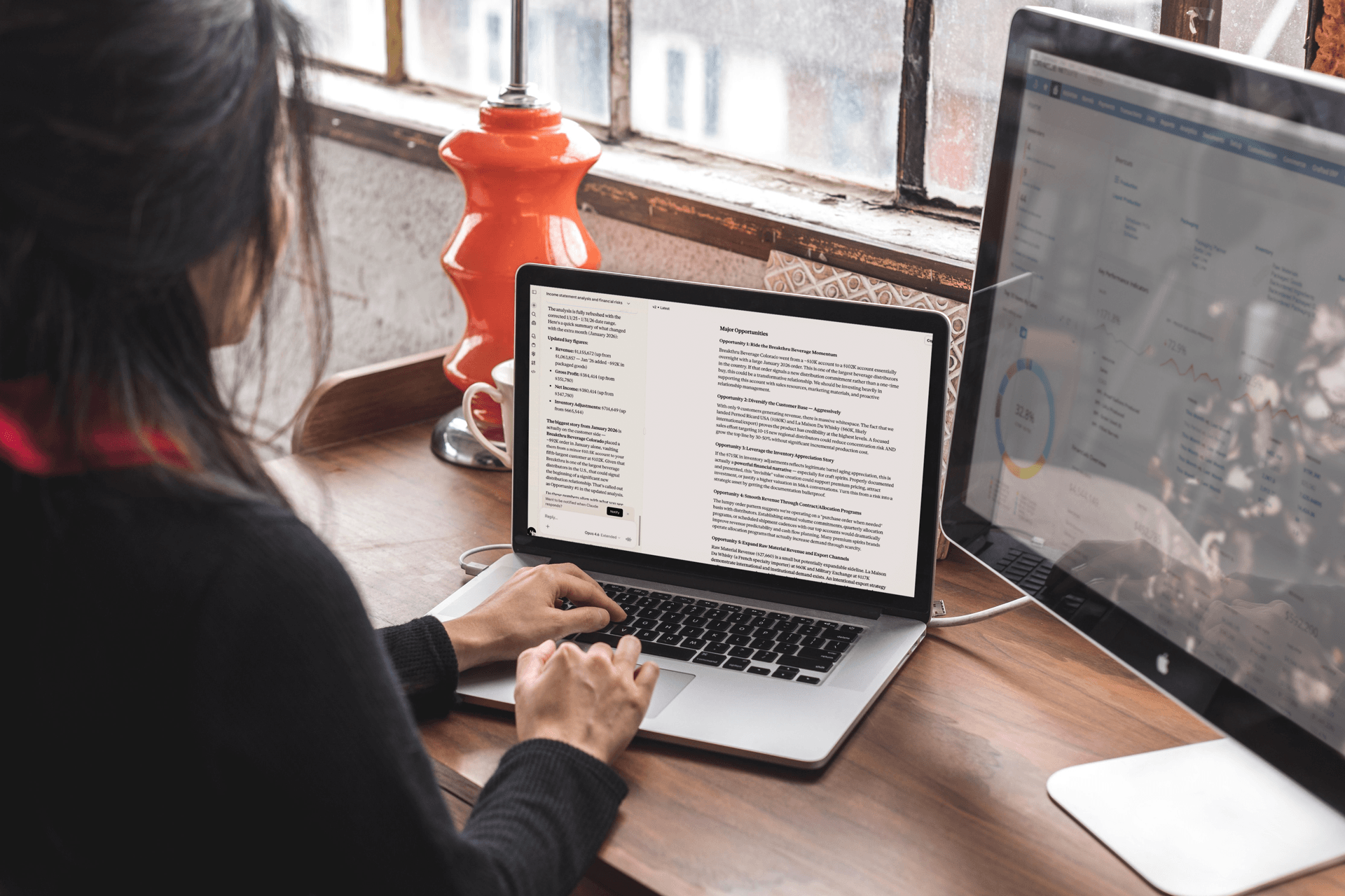 A photo of a woman with a laptop and external monitor on an office desk. She is working in Crafted ERP + NetSuite using new AI capabilities.