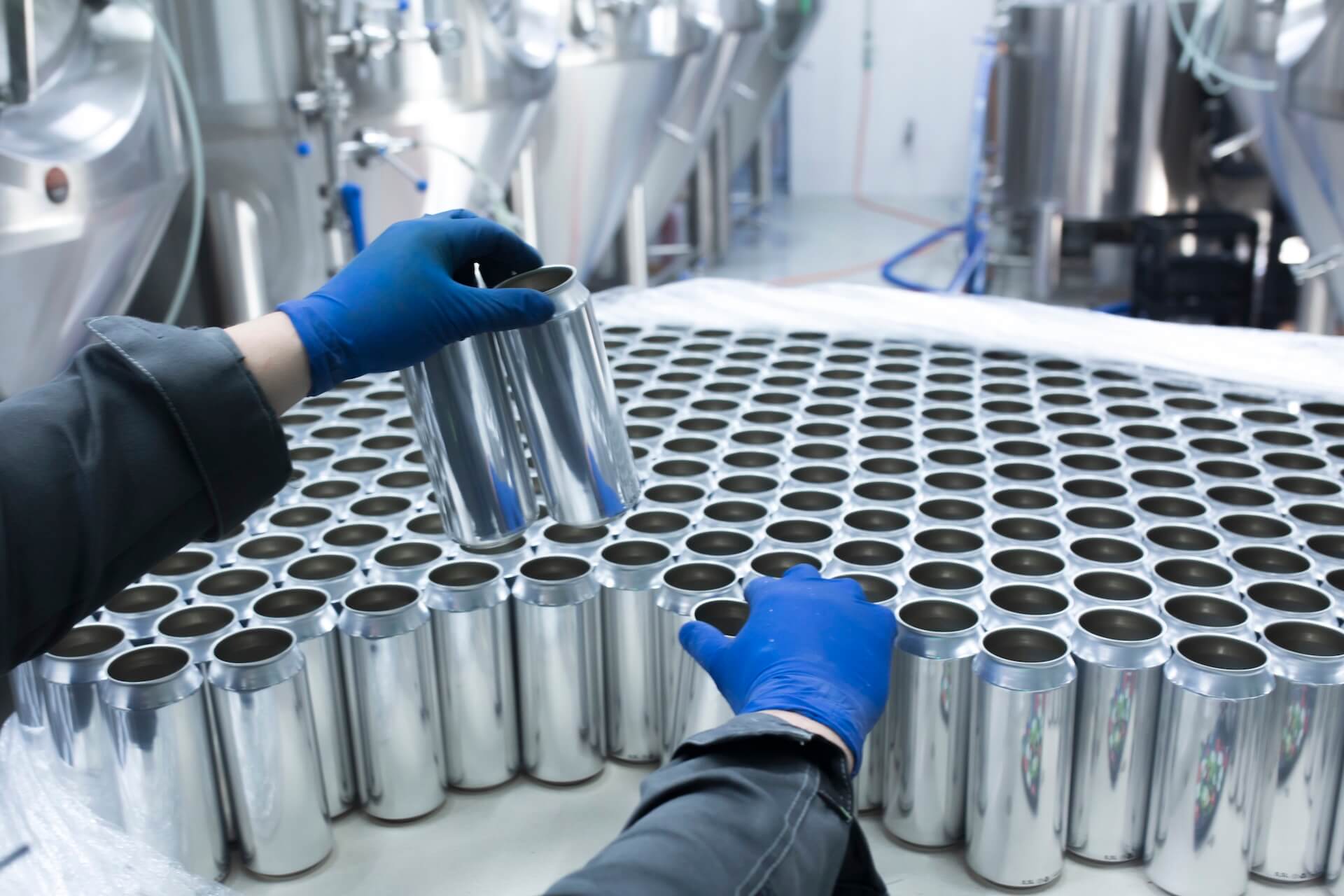 Beverage SaaS Solutions Blog Featured Image: brewery production floor, worker's hand taking new aluminum cans