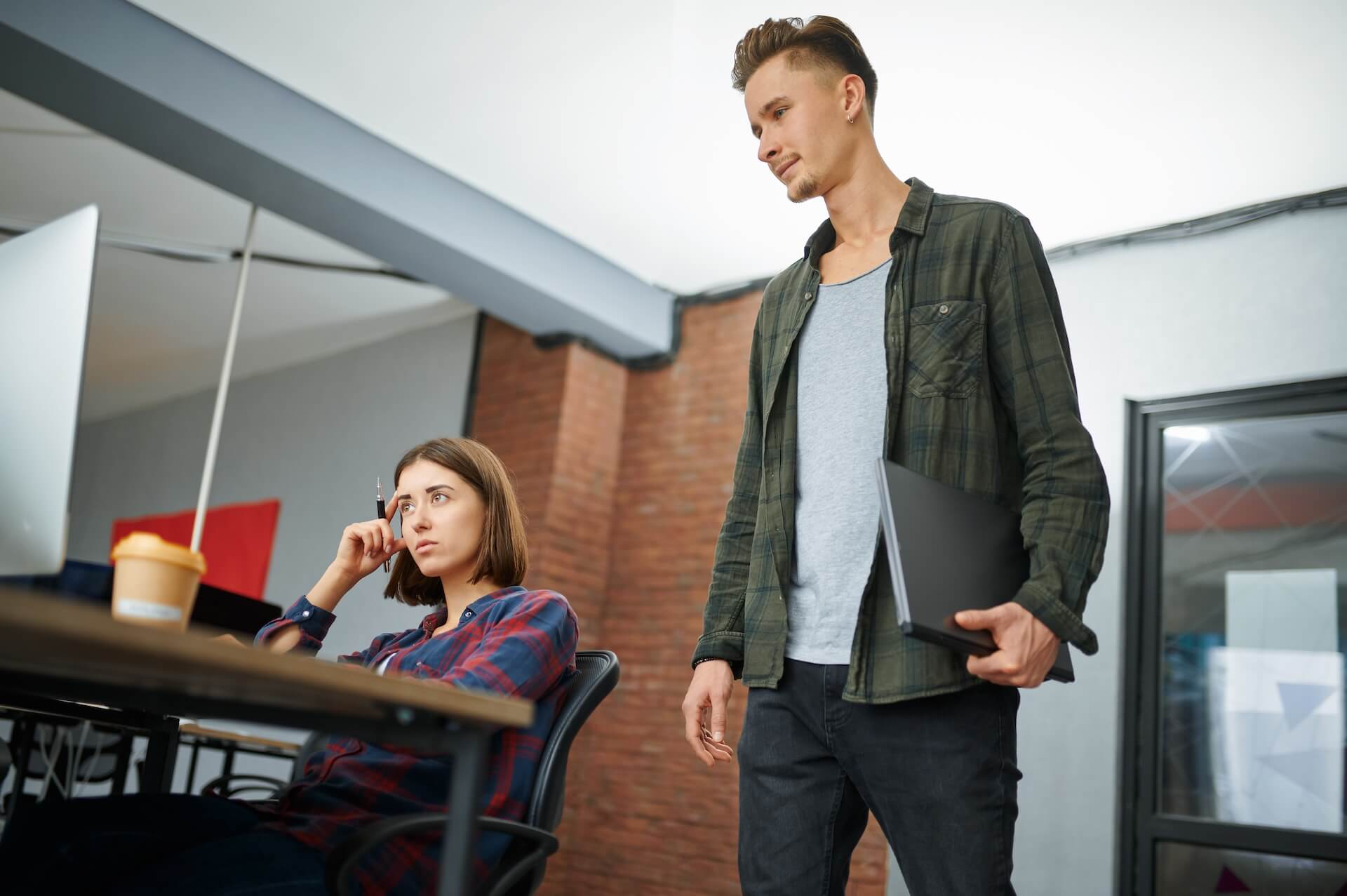 Male IT specialist holds laptop in brewery back office talking to female accounting specialist about the risks of unsupported ERP software.