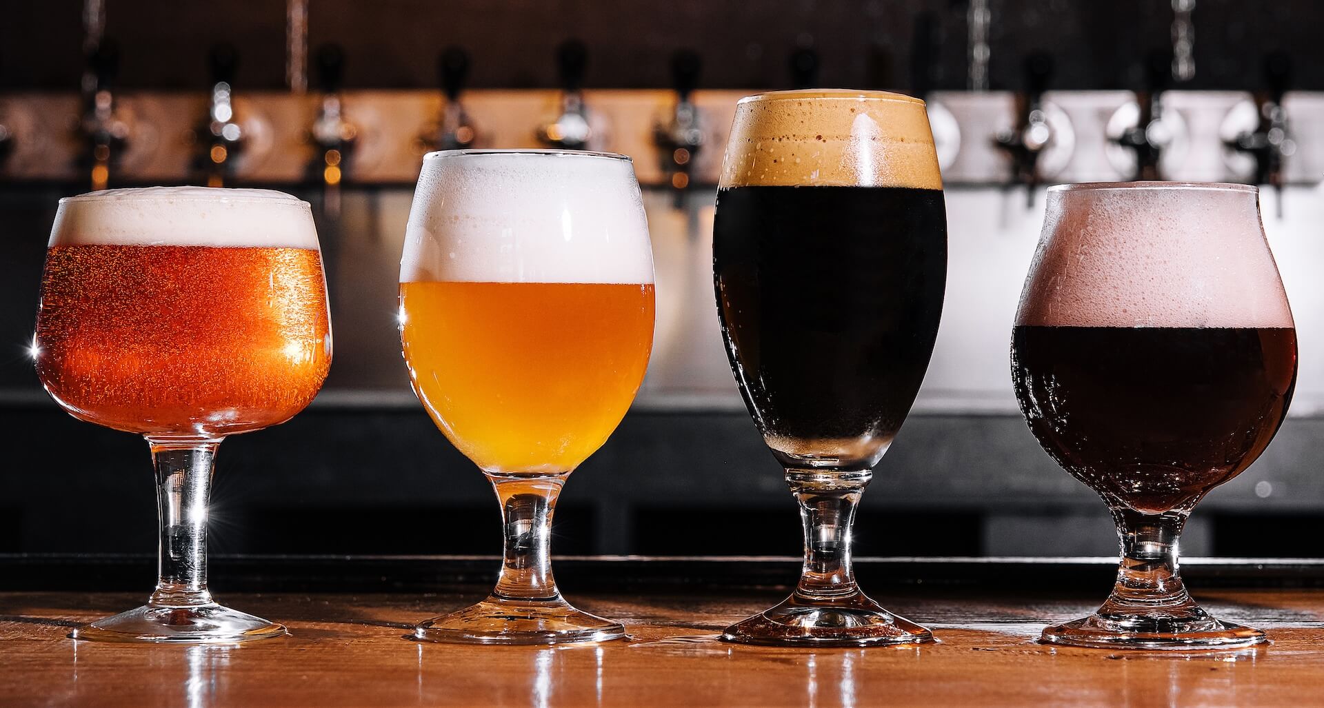 Different styles of beers in various types of glasses on a bar top